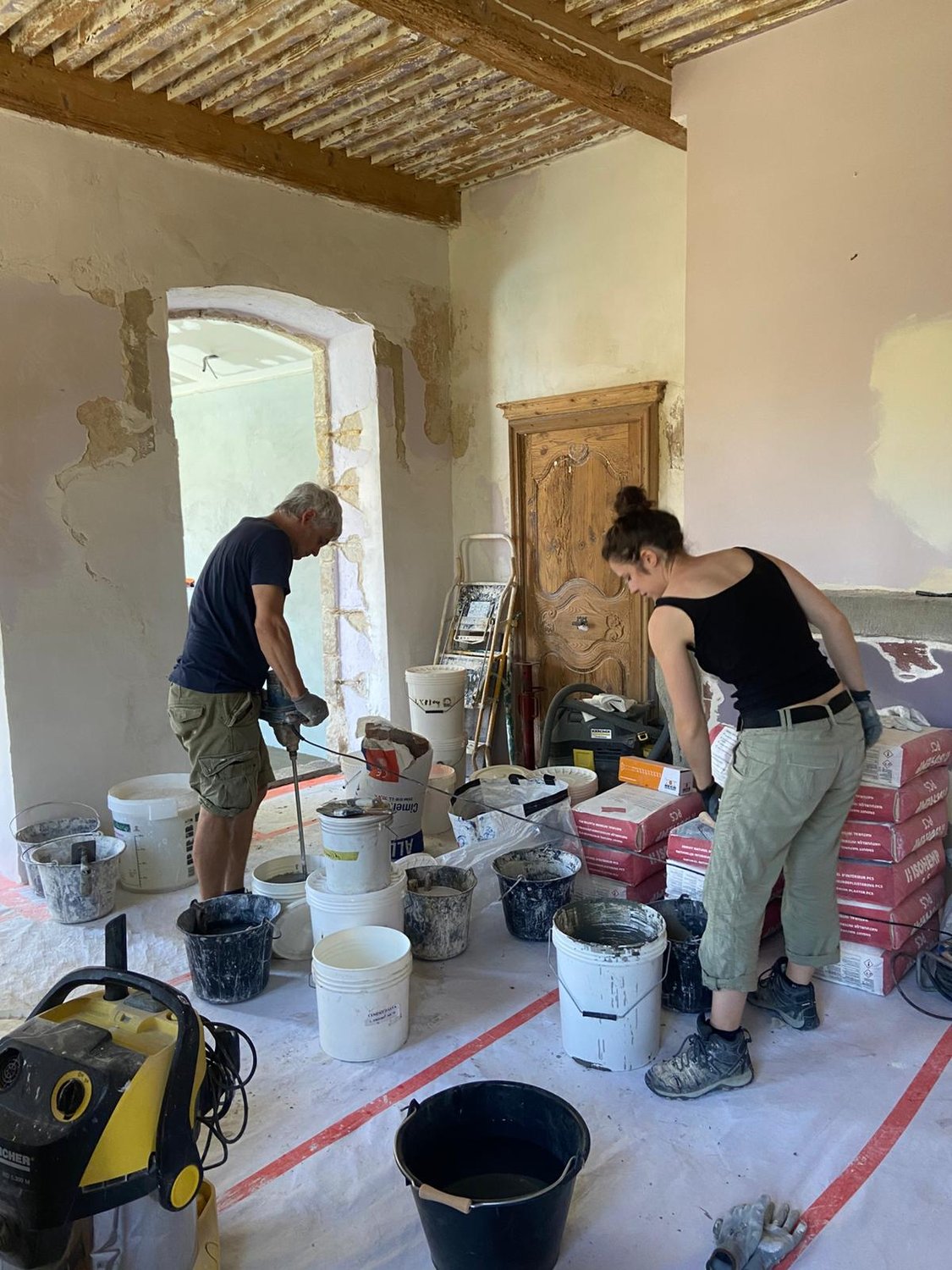 Lucile Wenger et un collègue préparant et appliquant l'enduit à la chaux dans une pièce en pierre