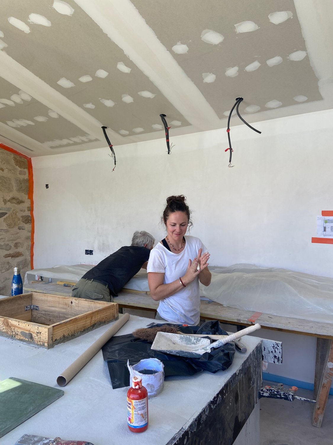 Lucile Wenger secouant la poussière de chaux de ses mains, outils de finition sur l'établi
